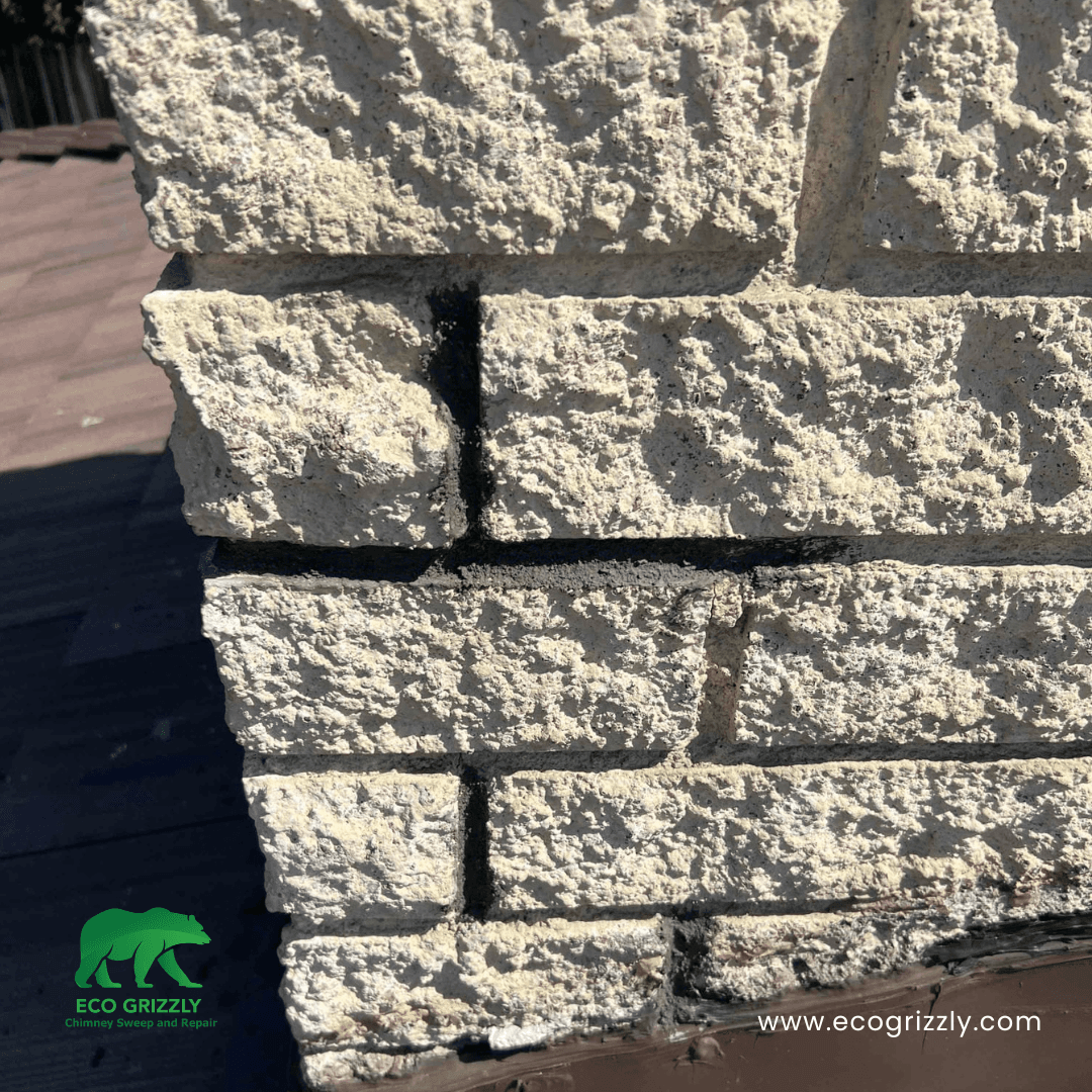 Light-colored brick chimney with dark mortar joints showing wear on a shingled roof