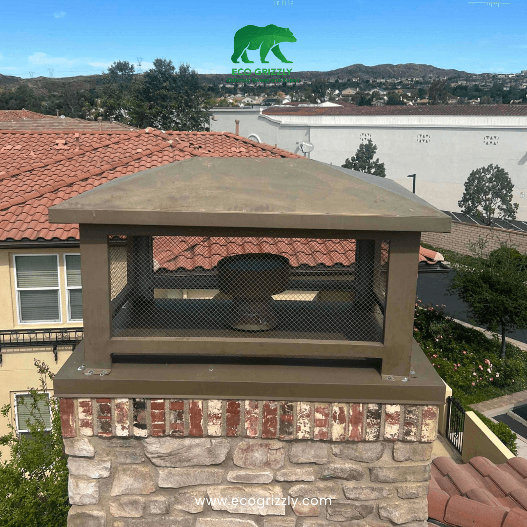 Bronze chimney cap with mesh sides on a stone and brick chimney with hills in background