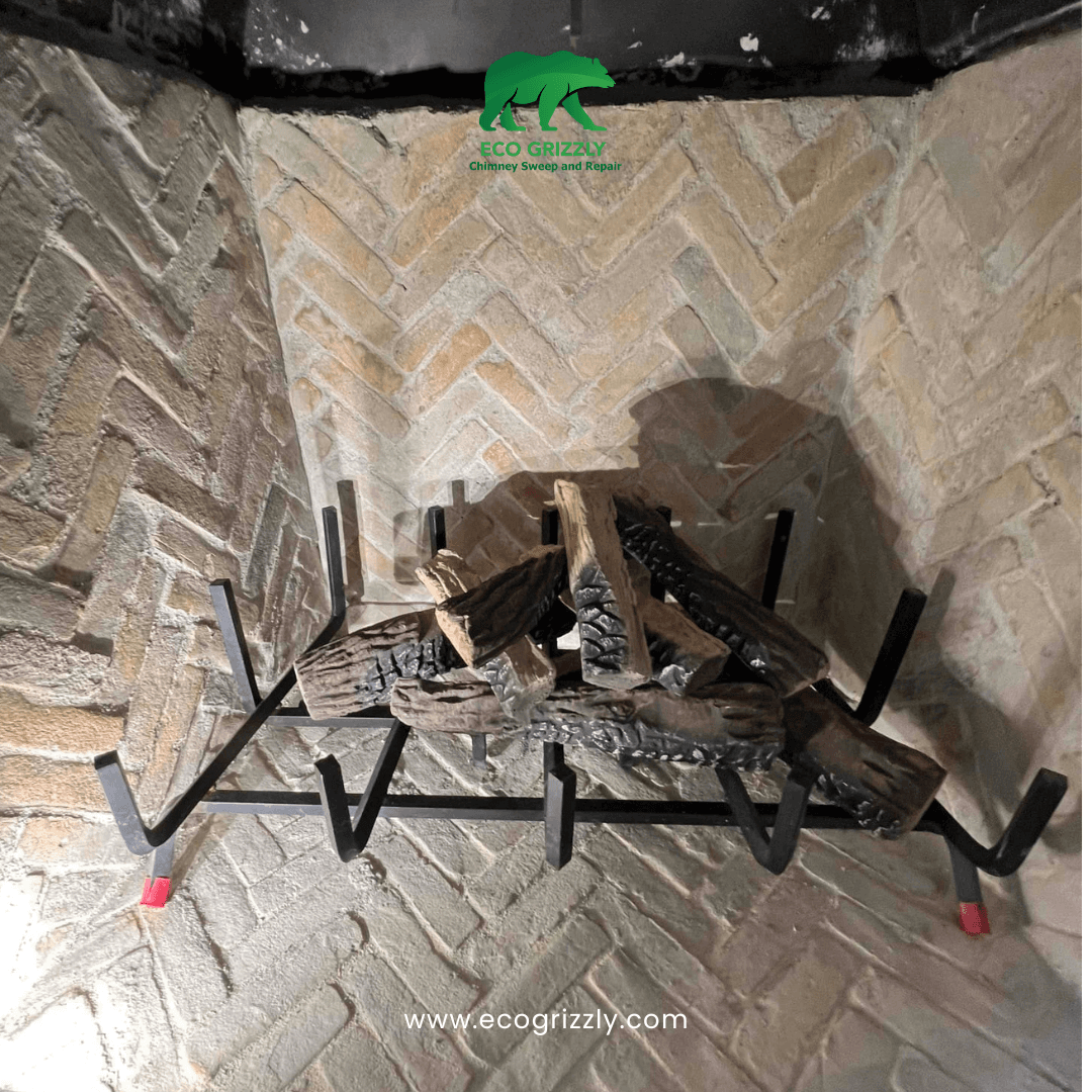Brick fireplace interior with herringbone pattern and metal grate holding artificial logs