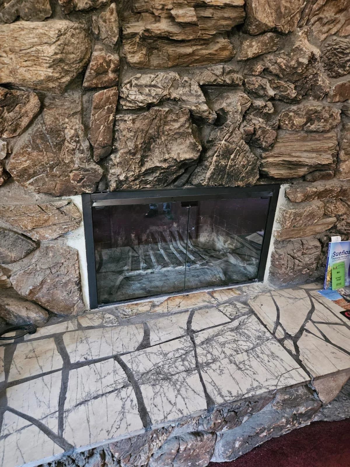 Completed fireplace glass door installation with matte black bi-fold frame on a masonry fireplace
