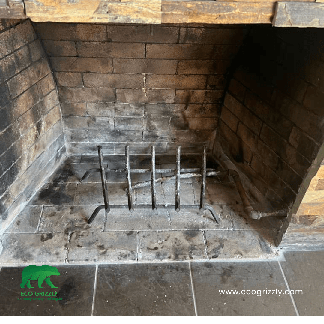 Brick fireplace interior with metal grate and visible soot buildup on hearth and walls
