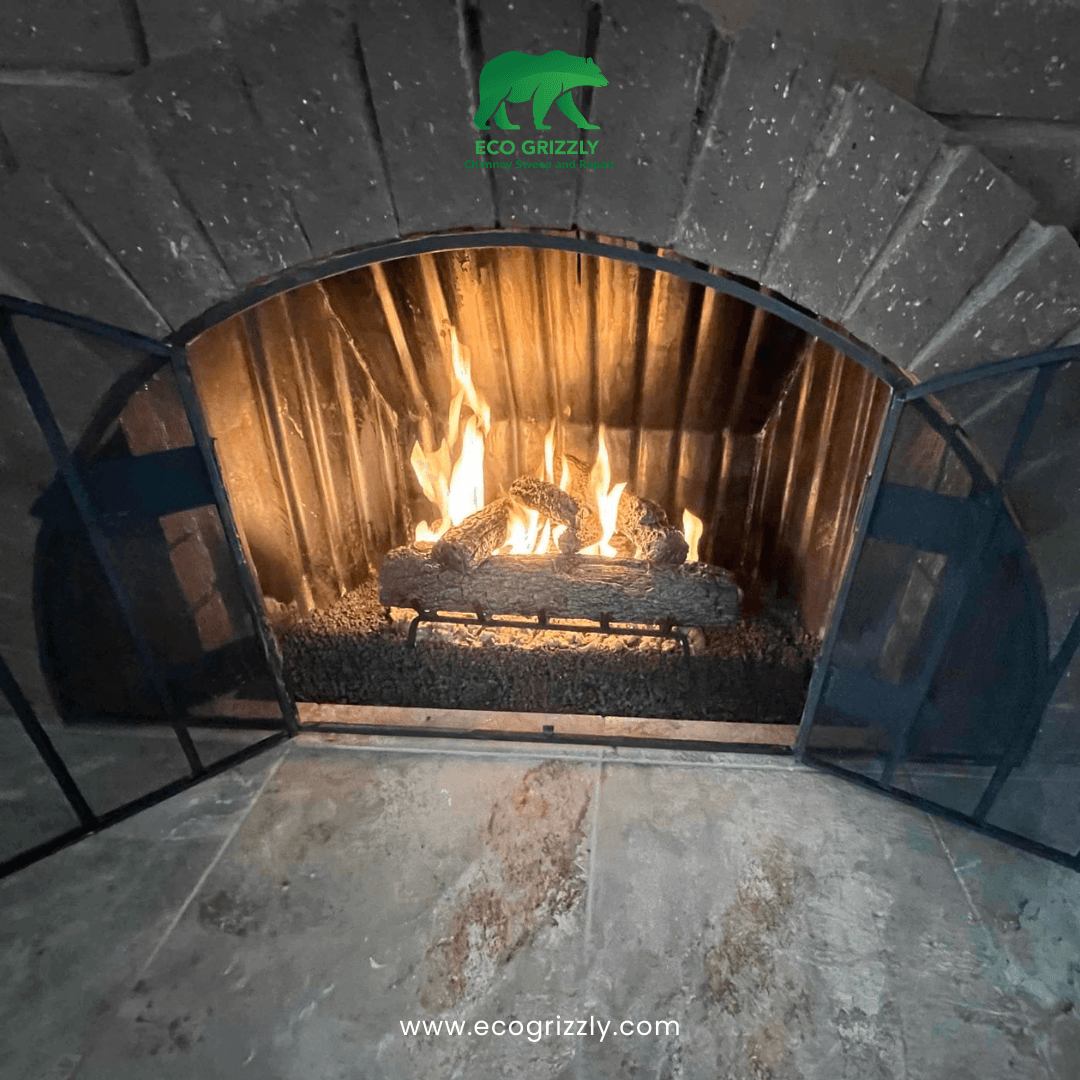 Arched brick fireplace with gas log set burning behind a metal screen