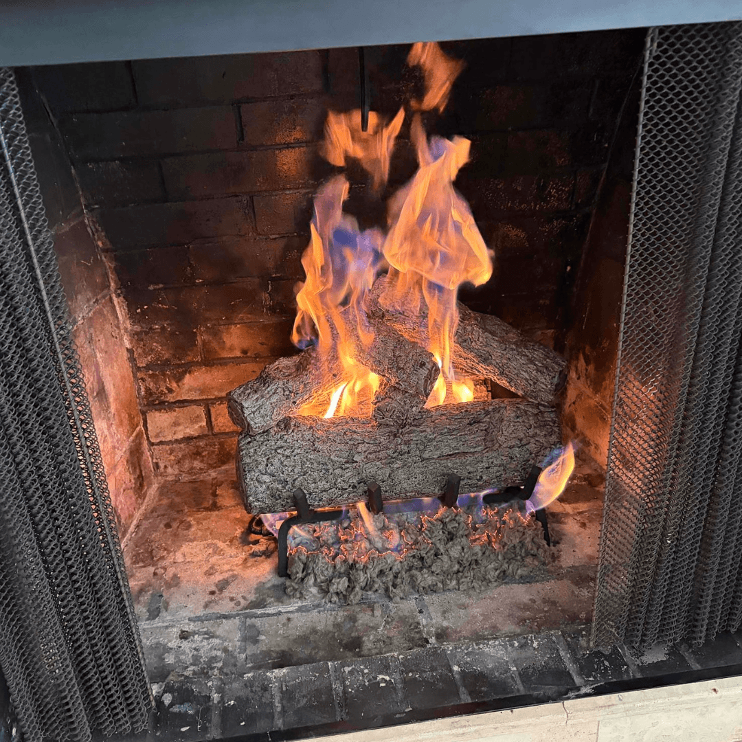 Gas logs burning in a fireplace with stone surround and mesh screen
