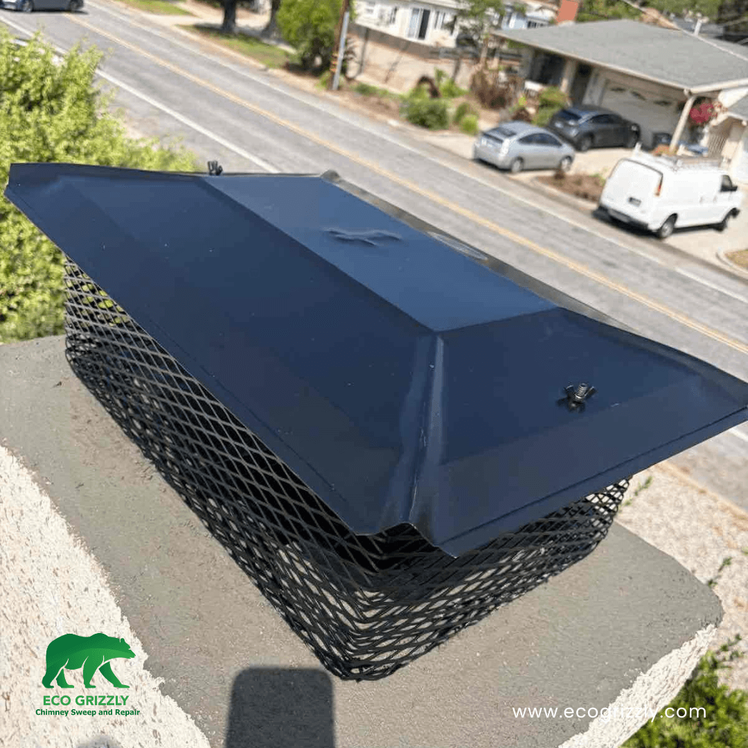 New black metal chimney cap with mesh sides on a concrete crown in a residential area