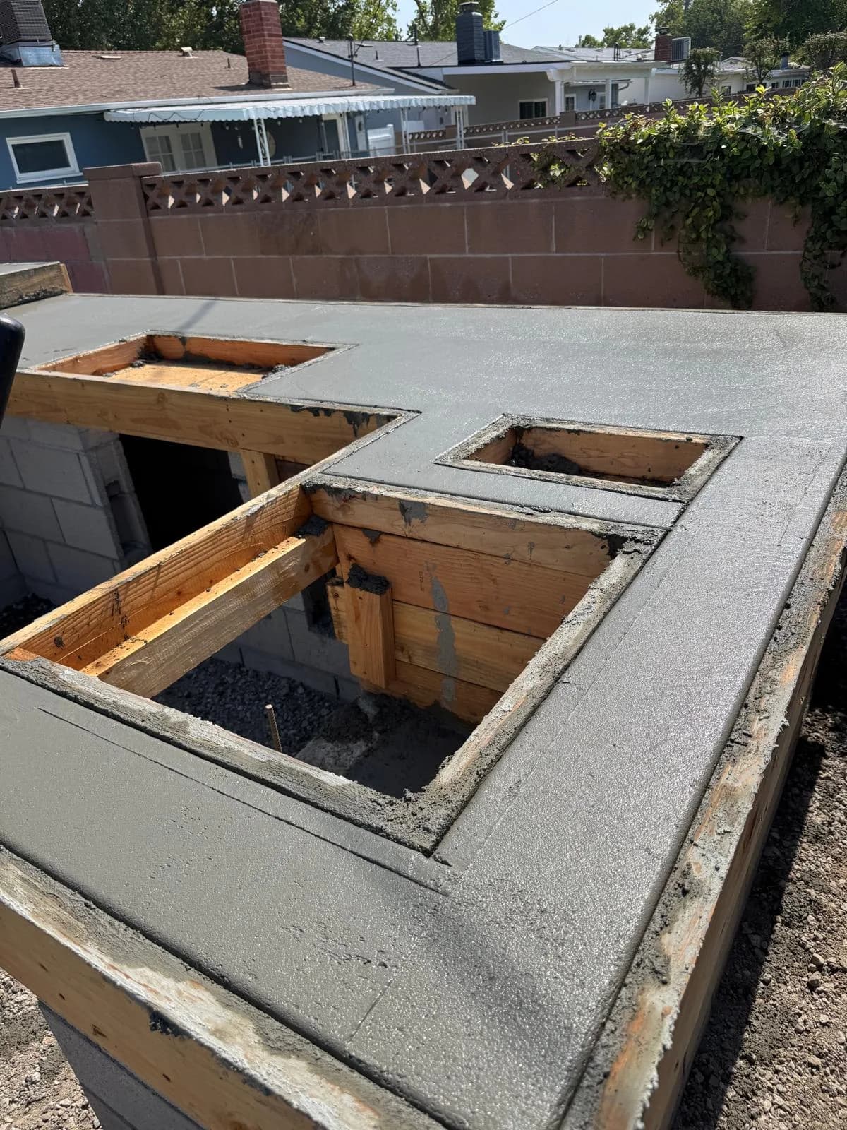 Fresh concrete poured over wood framing for an outdoor fireplace base with rectangular firebox openings