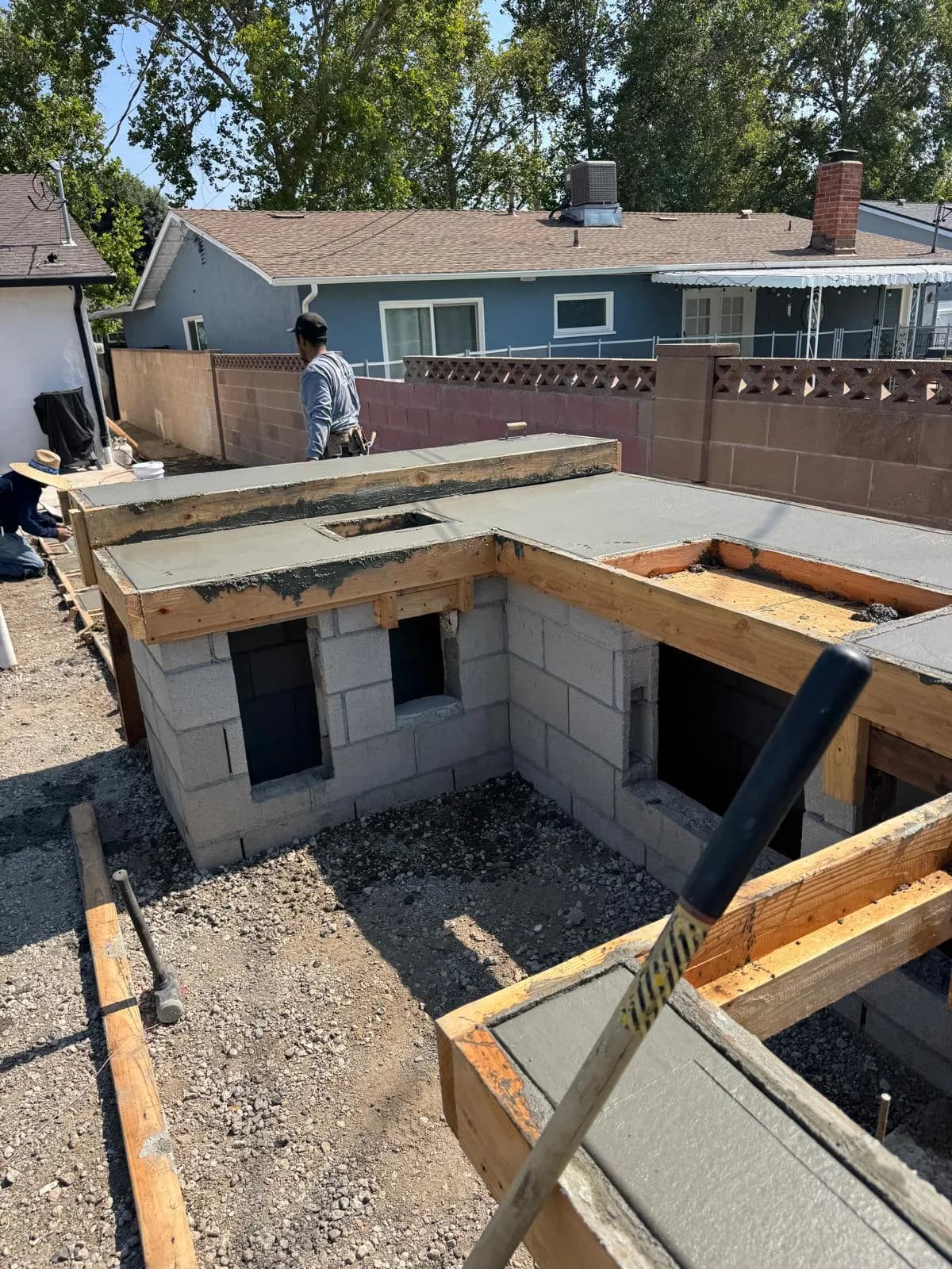 Concrete being poured over wood forms on a cinder block outdoor fireplace under construction