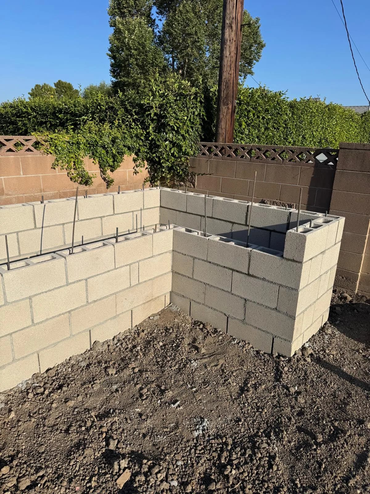 Cinder block fireplace structure under construction with exposed rebar in a backyard corner