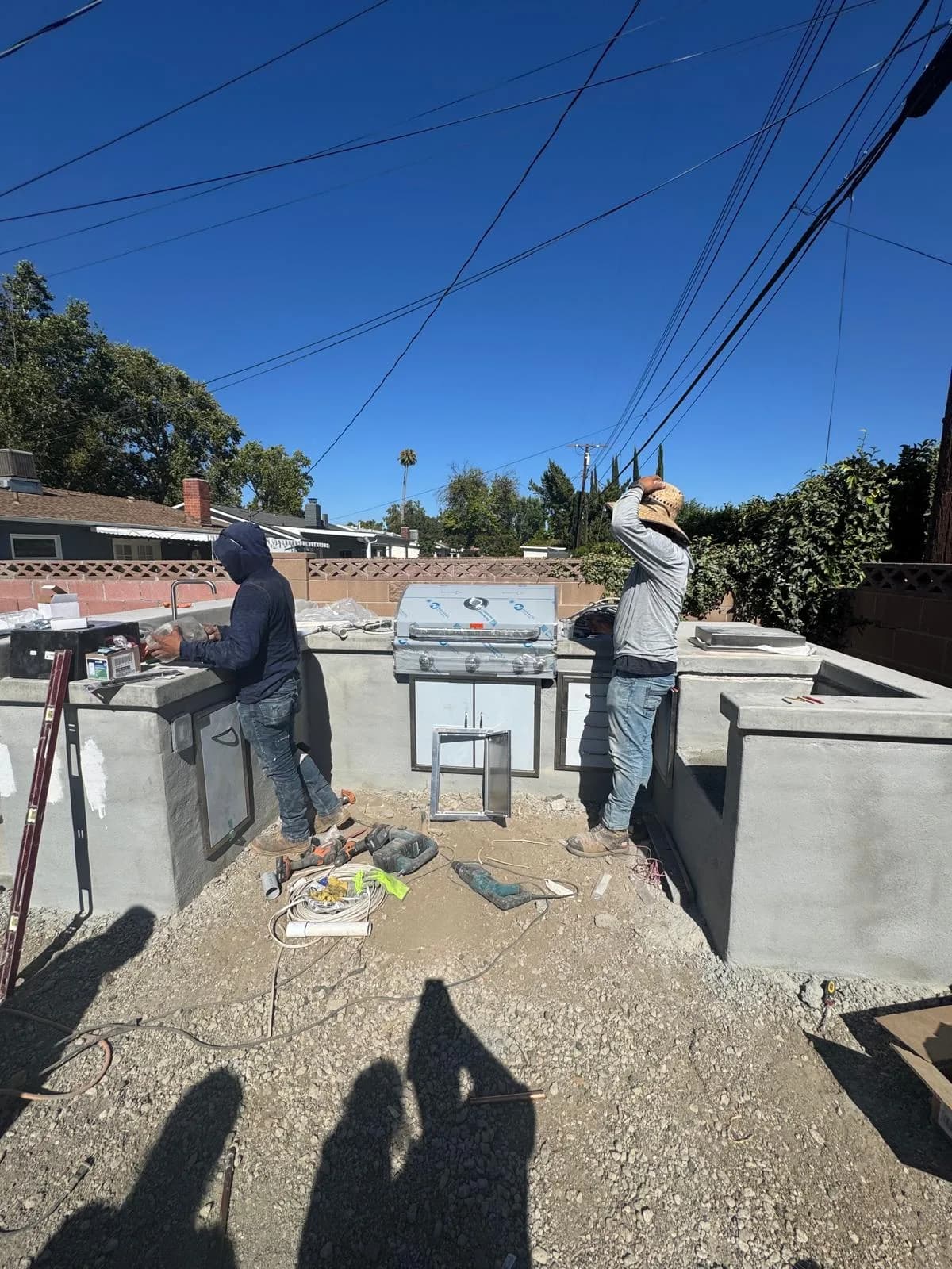 Two workers install an outdoor kitchen with a grill and concrete counters in a backyard