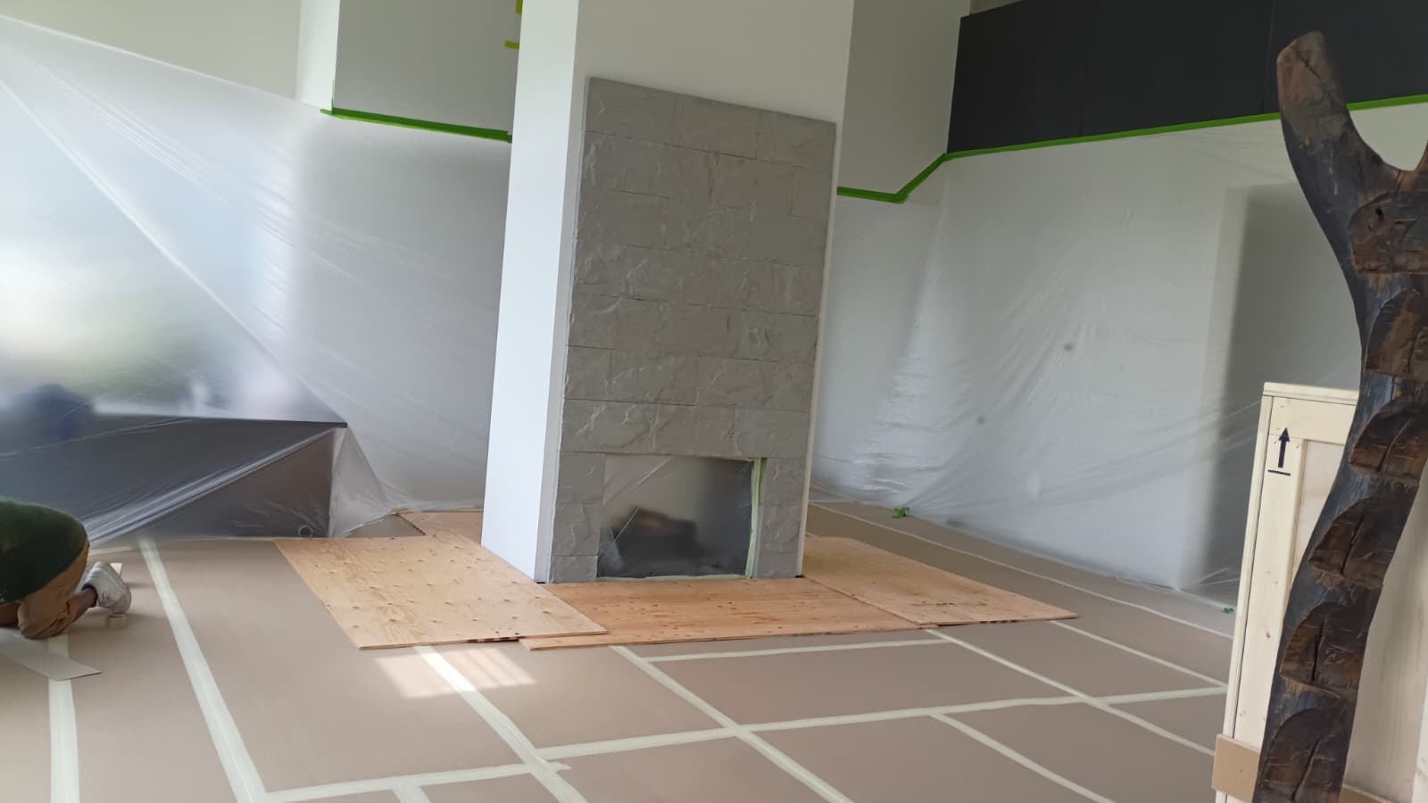 Great room masked in plastic sheeting with floor protection down around the original stone clad fireplace column