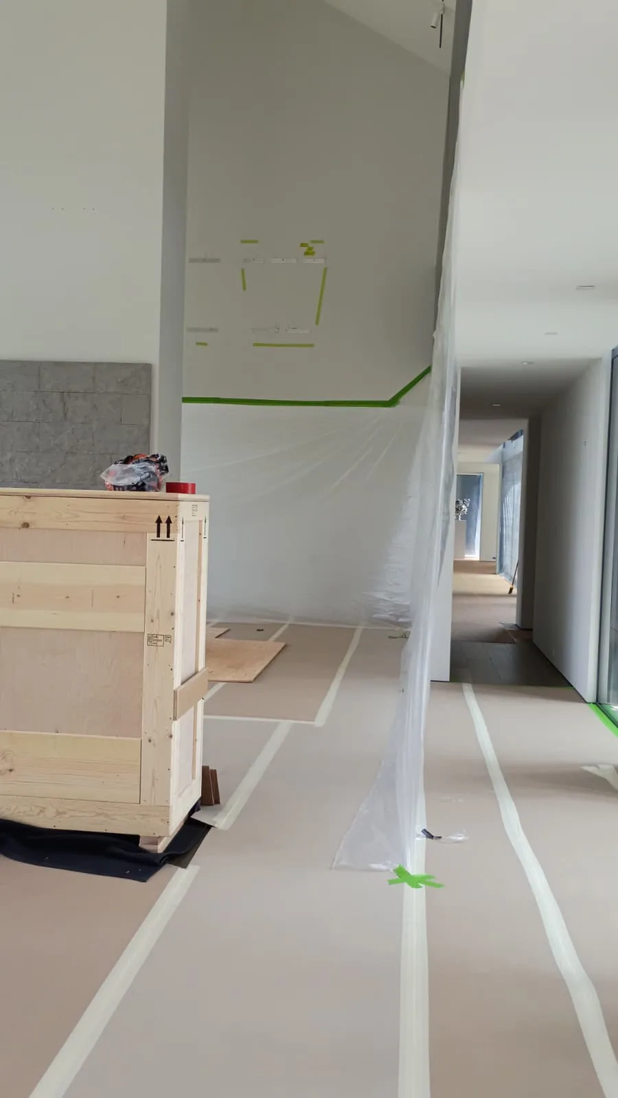 Hallway masked with plastic sheeting and protective floor paper with a crate of materials staged for the remodel