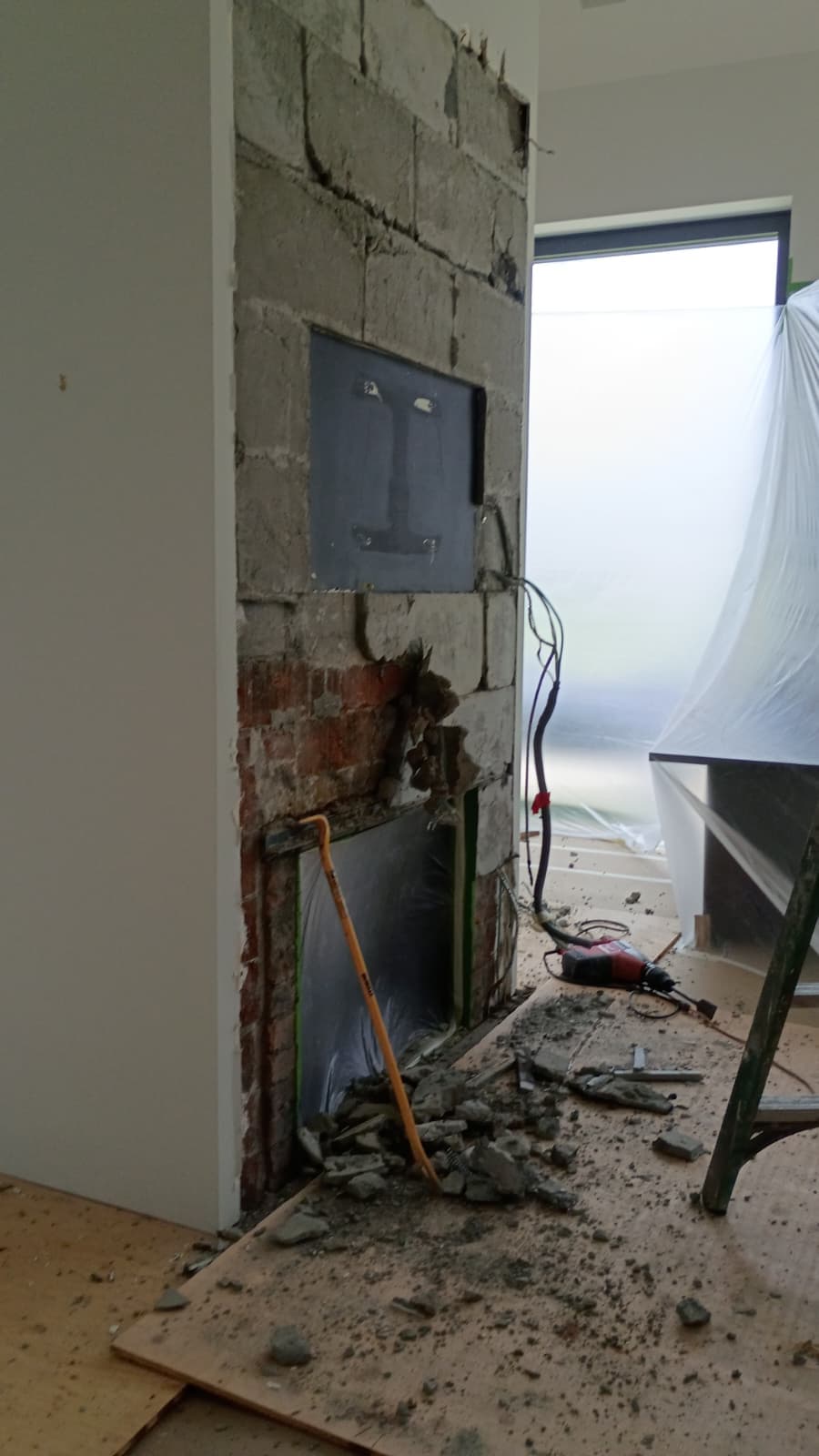 Fireplace stripped to concrete block and red brick with debris on the floor and the firebox opening exposed