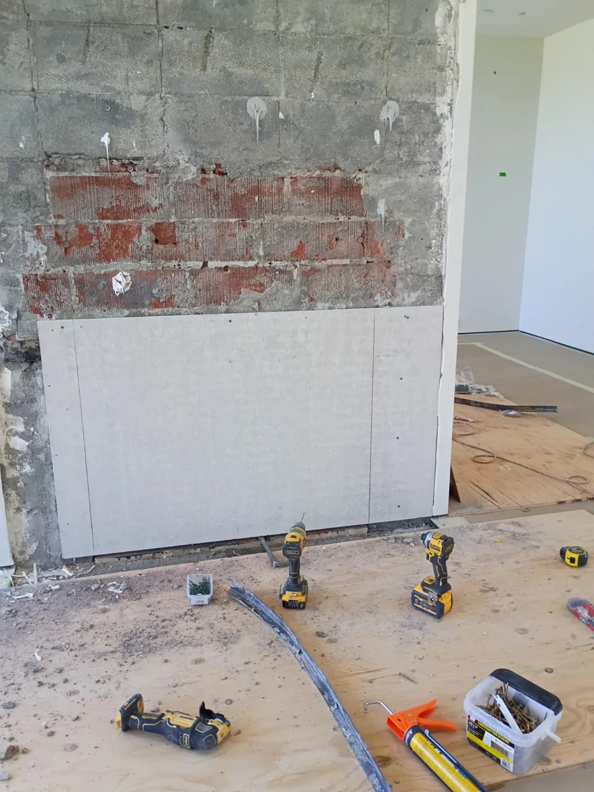 Chimney breast stripped to block and brick with the first new cement board panel set and tools on the floor