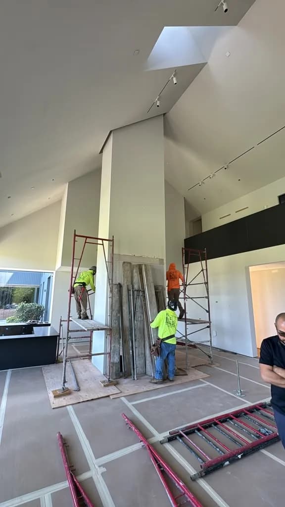 Scaffolding going up in the double height great room with two crew members preparing the fireplace column