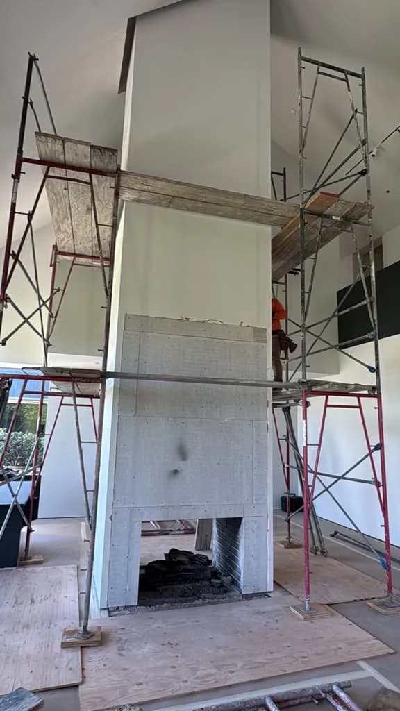 Full height scaffolding erected around the boarded fireplace column in the vaulted great room