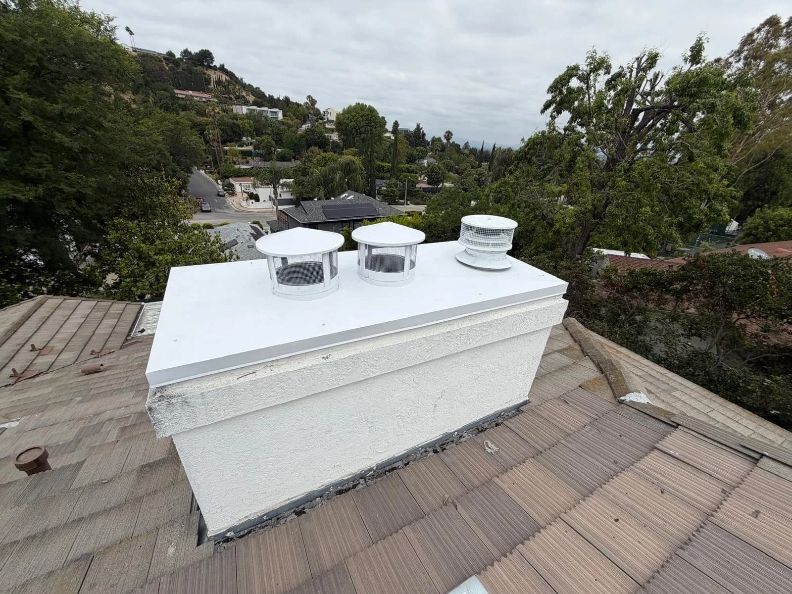Finished white sheet metal chase cover with new flue caps on the stucco chimney above a tile roof