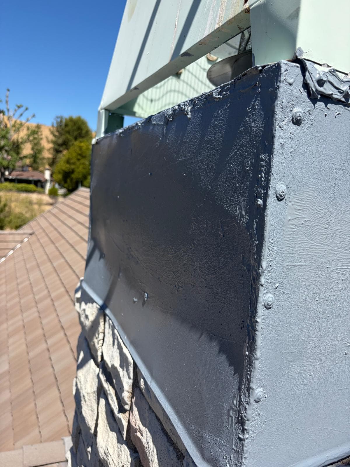 Sealant applied along the chase cover edge where it meets the stone chimney masonry