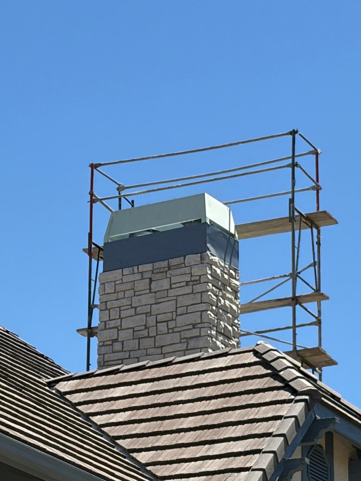 Wide view of the two-story chimney with scaffolding in place and corrected chase cover and shroud installed