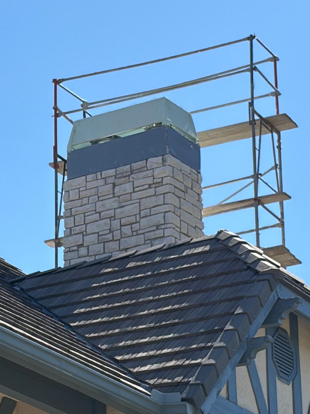 Scaffolding erected around a two-story stone chimney to safely access the chase cover and shroud for repair