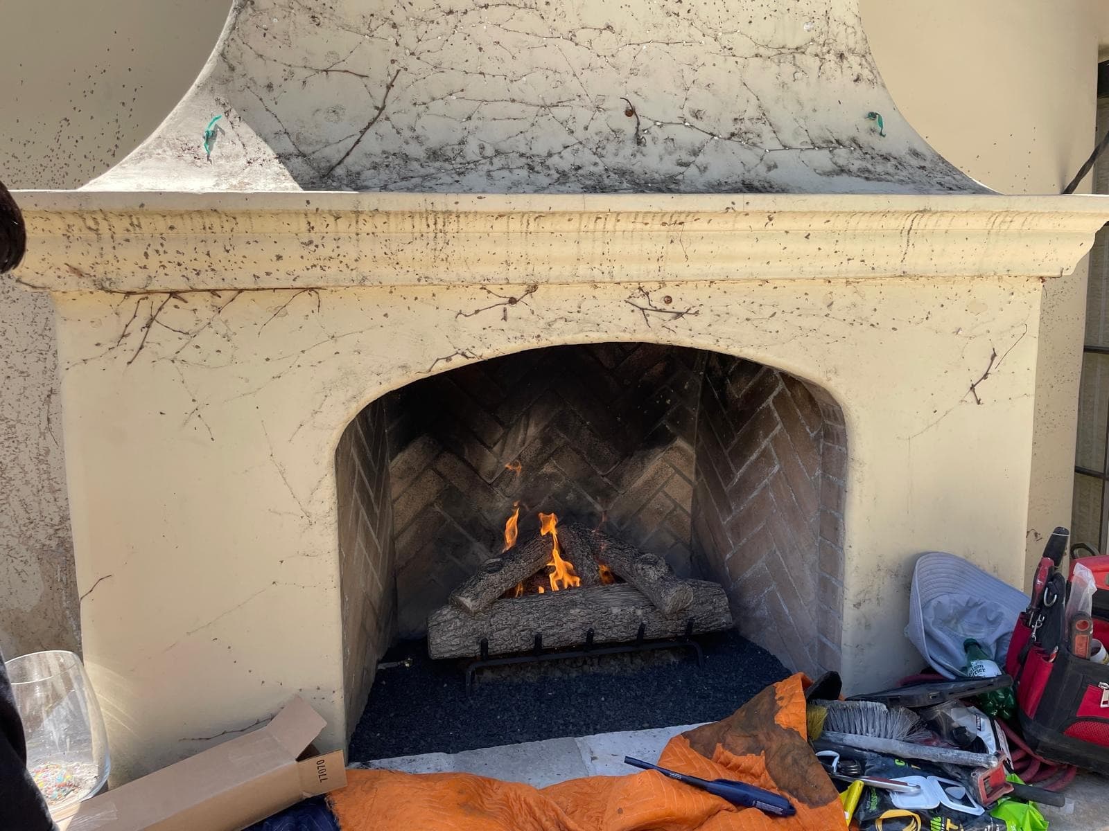 Lit gas logs on a black grate inside a tall arched stone fireplace with a herringbone brick firebox