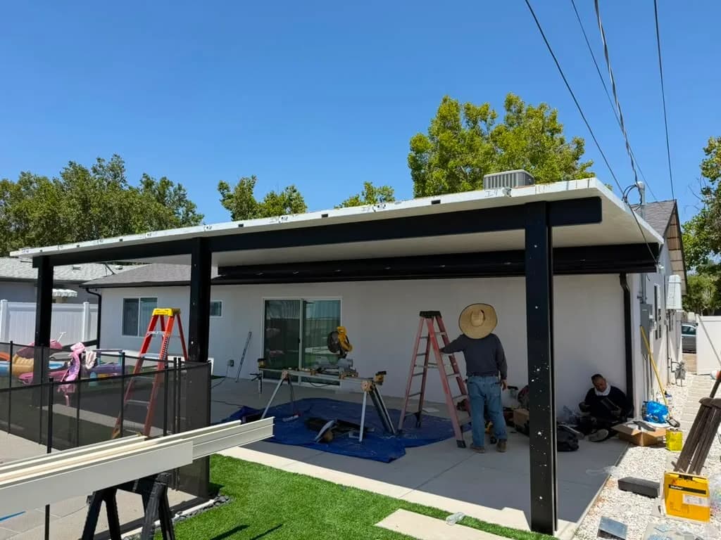 Crew on ladders installing the aluminum patio cover frame beside the pool on a clear day