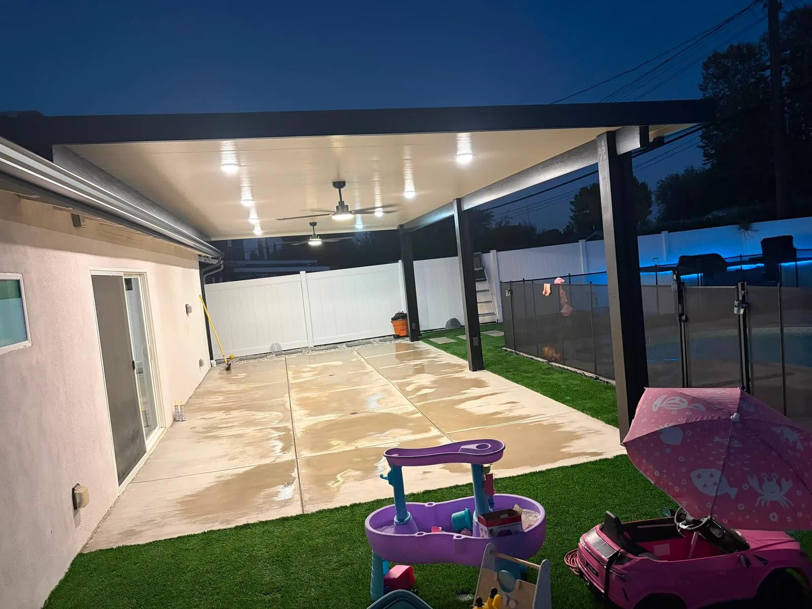Recessed lights and two ceiling fans glowing under the new patio cover above the concrete patio at night