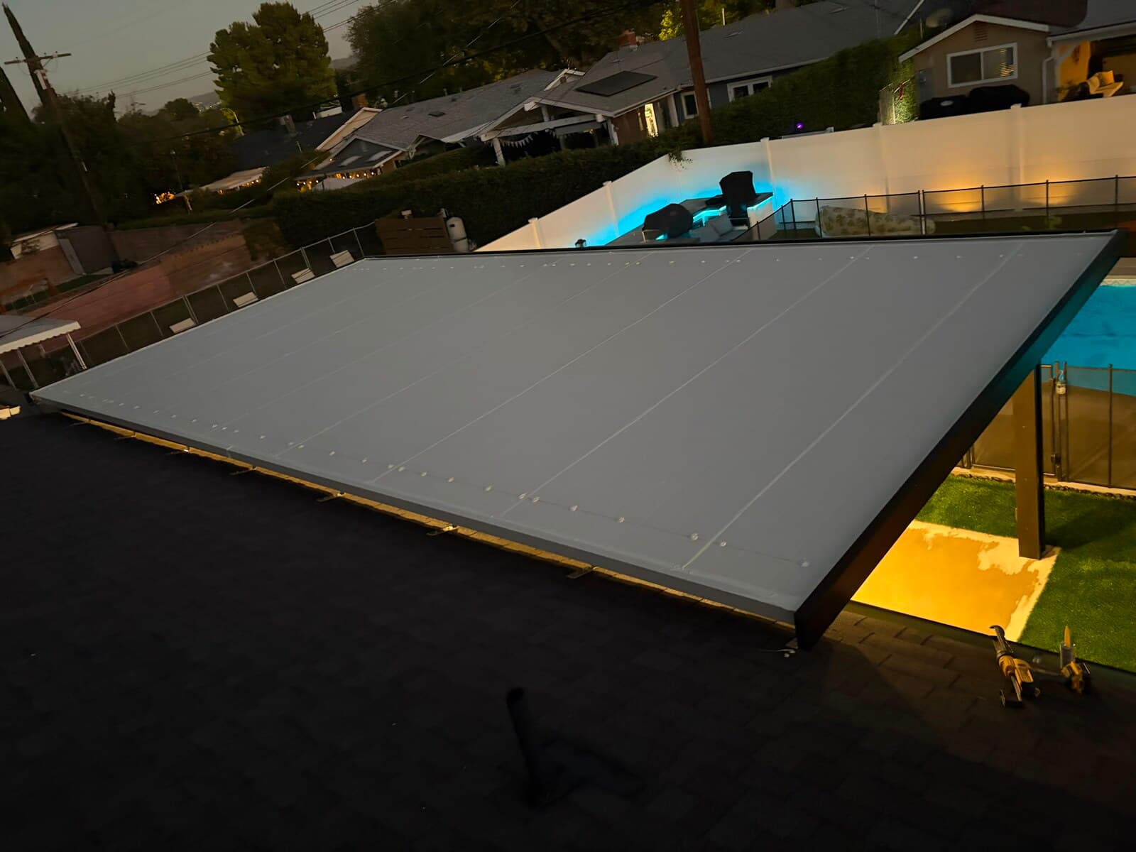 Overhead view of the finished patio cover panels with the lit backyard and pool beyond at dusk