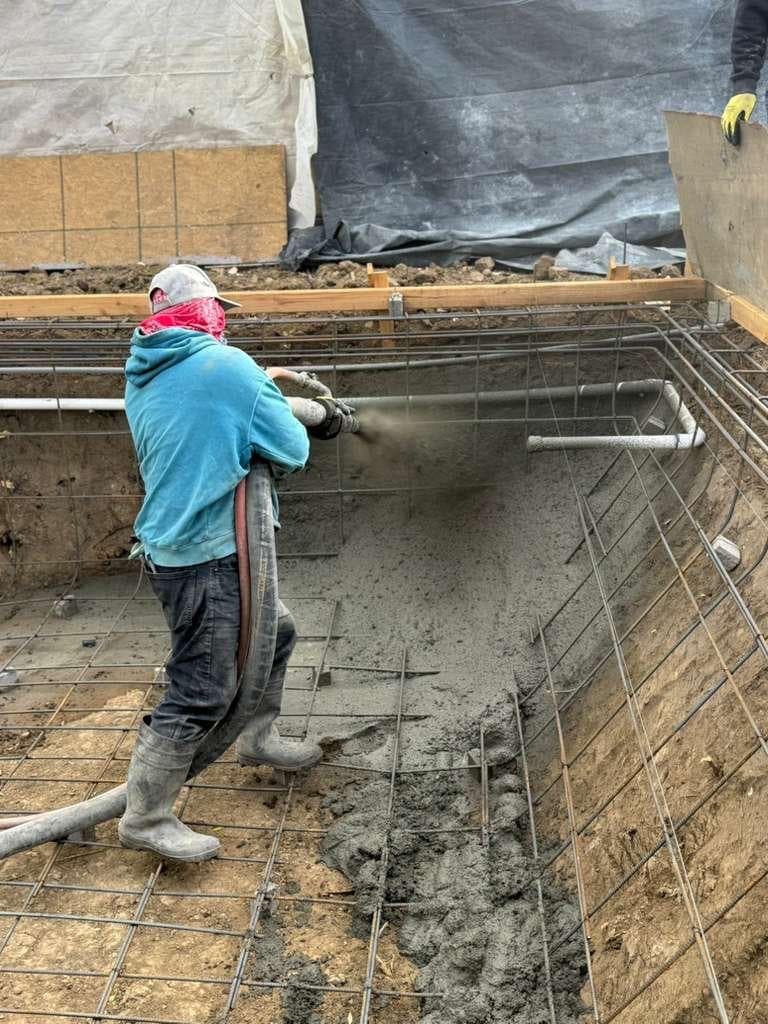 Worker spraying gunite shotcrete onto rebar cage to form pool shell