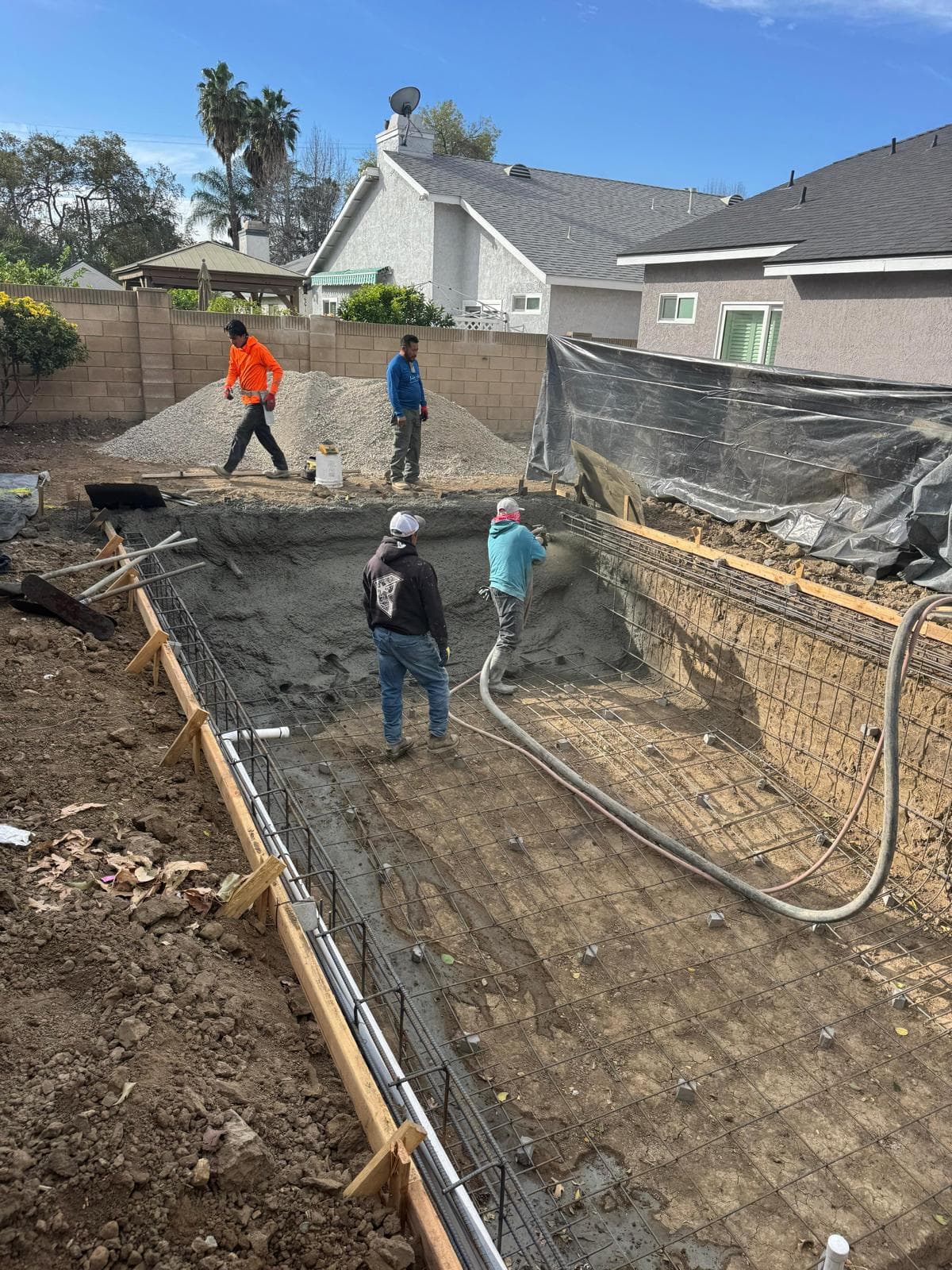 Crew spraying gunite across full pool shell with rebar cage visible