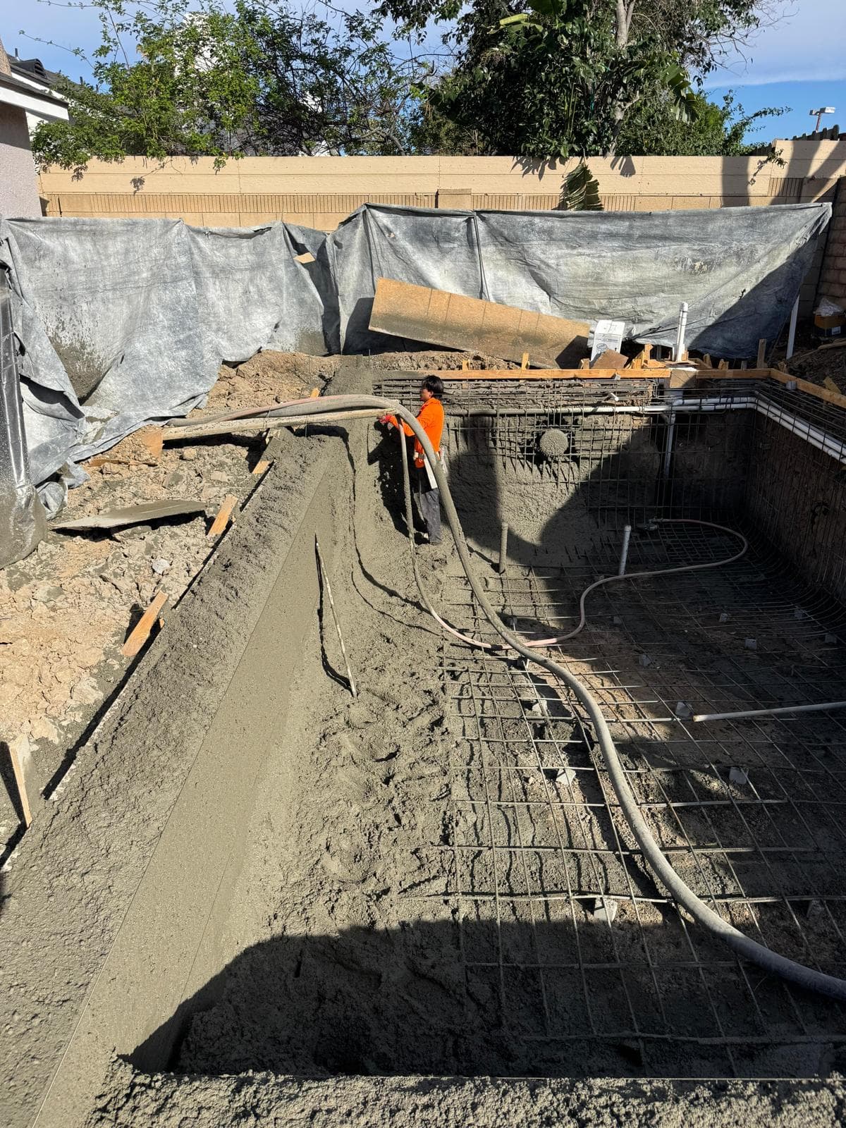 Worker pouring and finishing concrete bond beam around pool perimeter