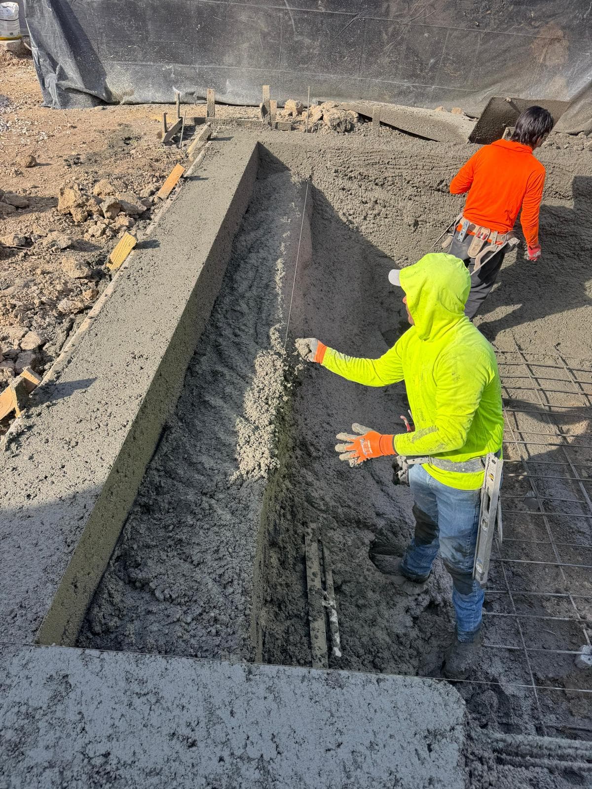 Workers troweling concrete bench form inside pool shell