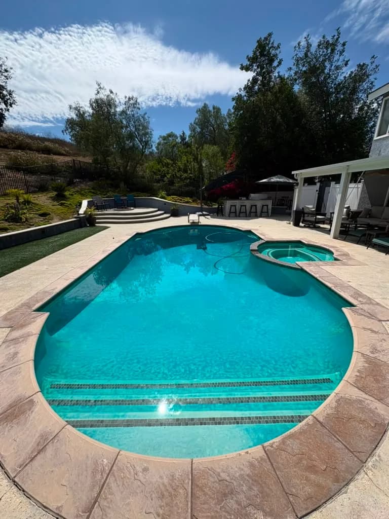 Freeform pool and raised spa before the remodel with aged mottled plaster and dark waterline tile