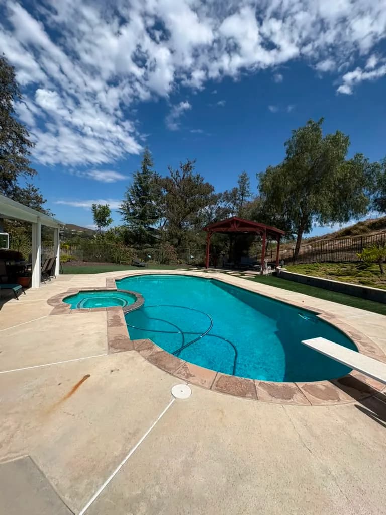 Wide view of the backyard pool and spa before replastering with the gazebo and hillside behind