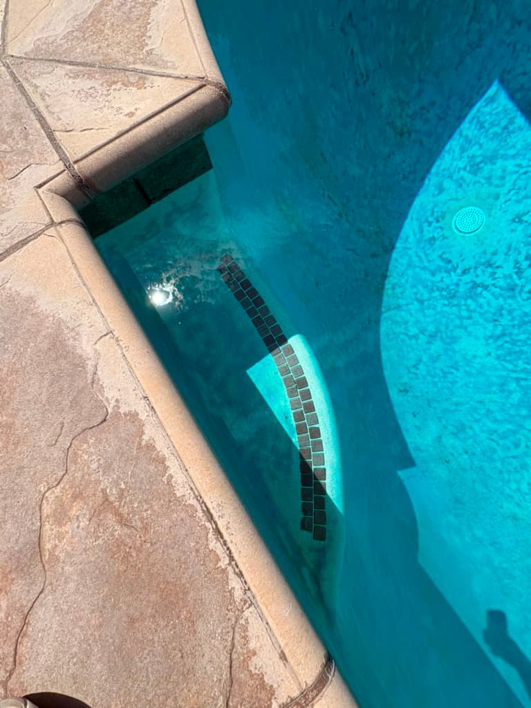 Close view of the pool step and waterline showing dark square tile and discolored plaster