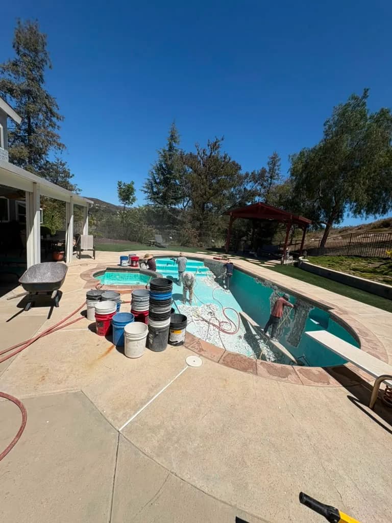 Plaster buckets and hoses staged on the deck while the crew applies new plaster in the pool