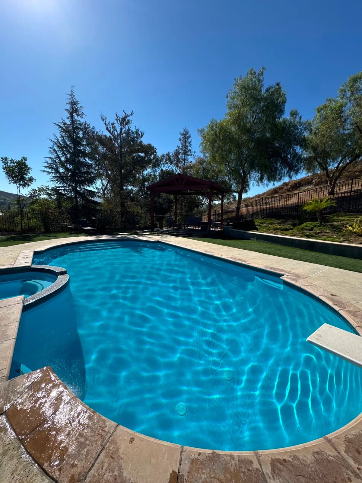 Completed pool remodel filled with clear blue water below the gazebo and hillside