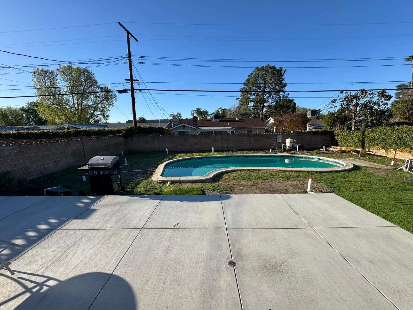 Backyard pool with water remaining during remodel, viewed from a concrete patio