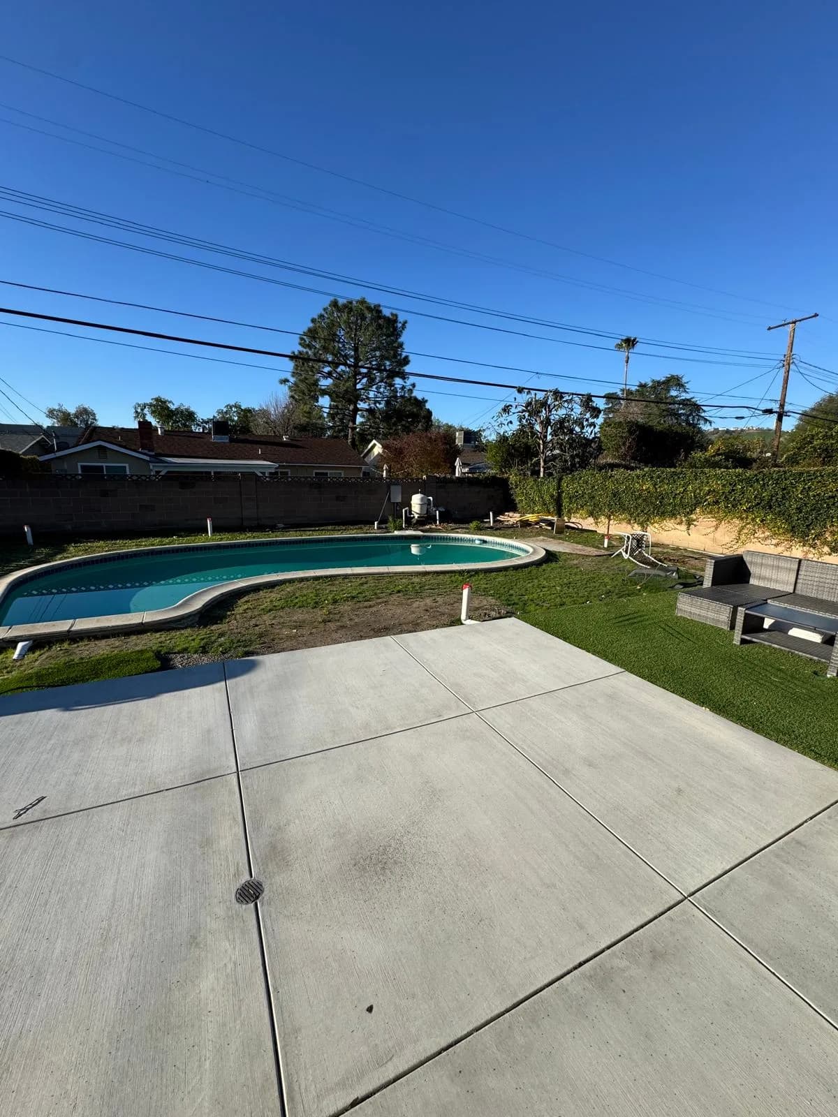 Backyard pool beside a new concrete patio with grass, outdoor seating, and a block wall fence
