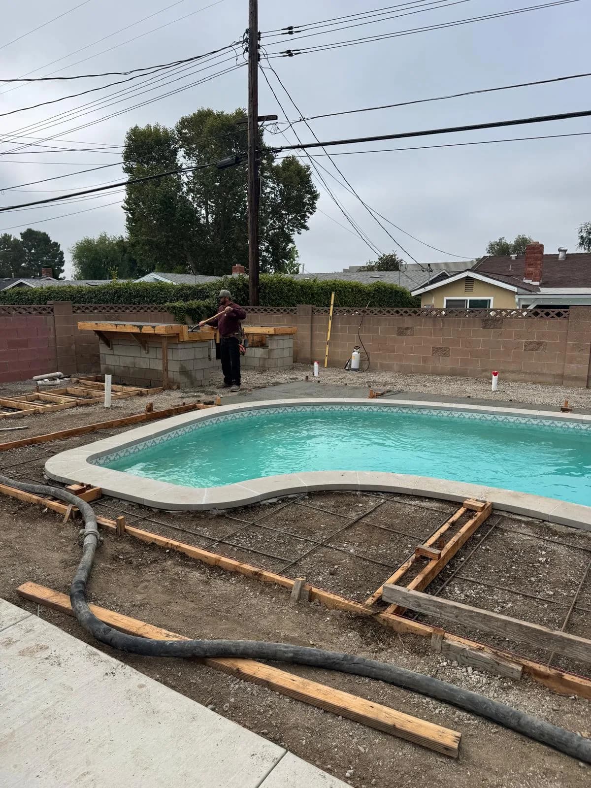 Refinished backyard pool with new coping and tile as a worker stands by a block outdoor bar under construction