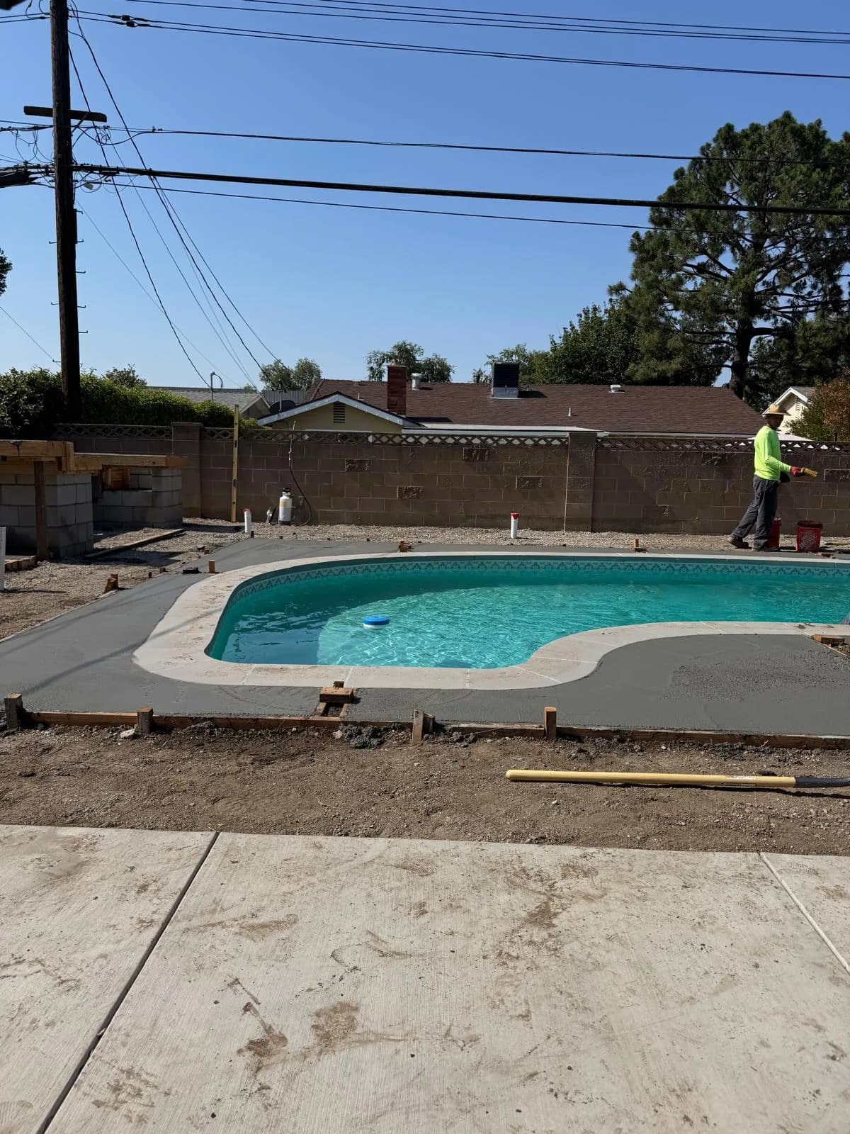 Worker finishes fresh concrete decking around a residential pool during a pool remodel