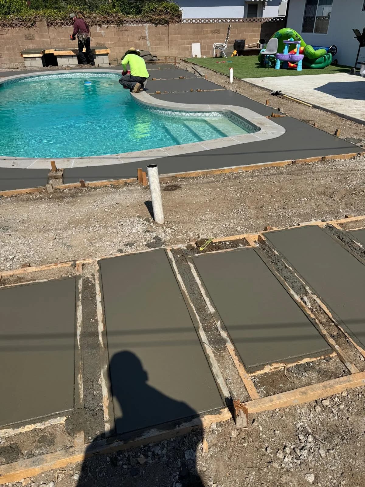 Workers finish new concrete decking around a residential pool during a backyard pool remodel