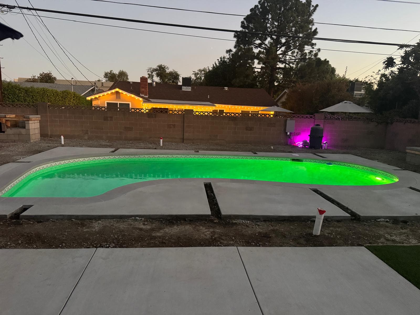 Refinished backyard pool glowing green at dusk with new coping and concrete deck sections in progress