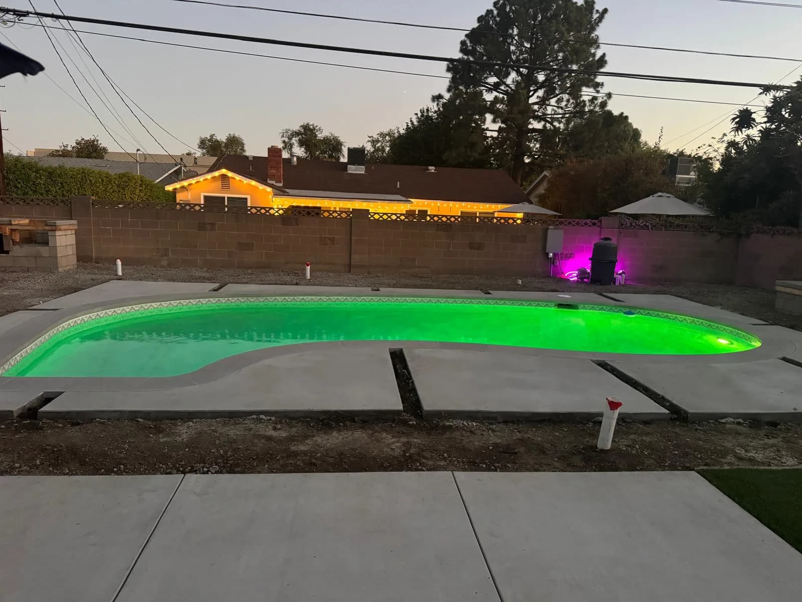 Refinished backyard pool glowing green at dusk with new coping and concrete deck sections in progress