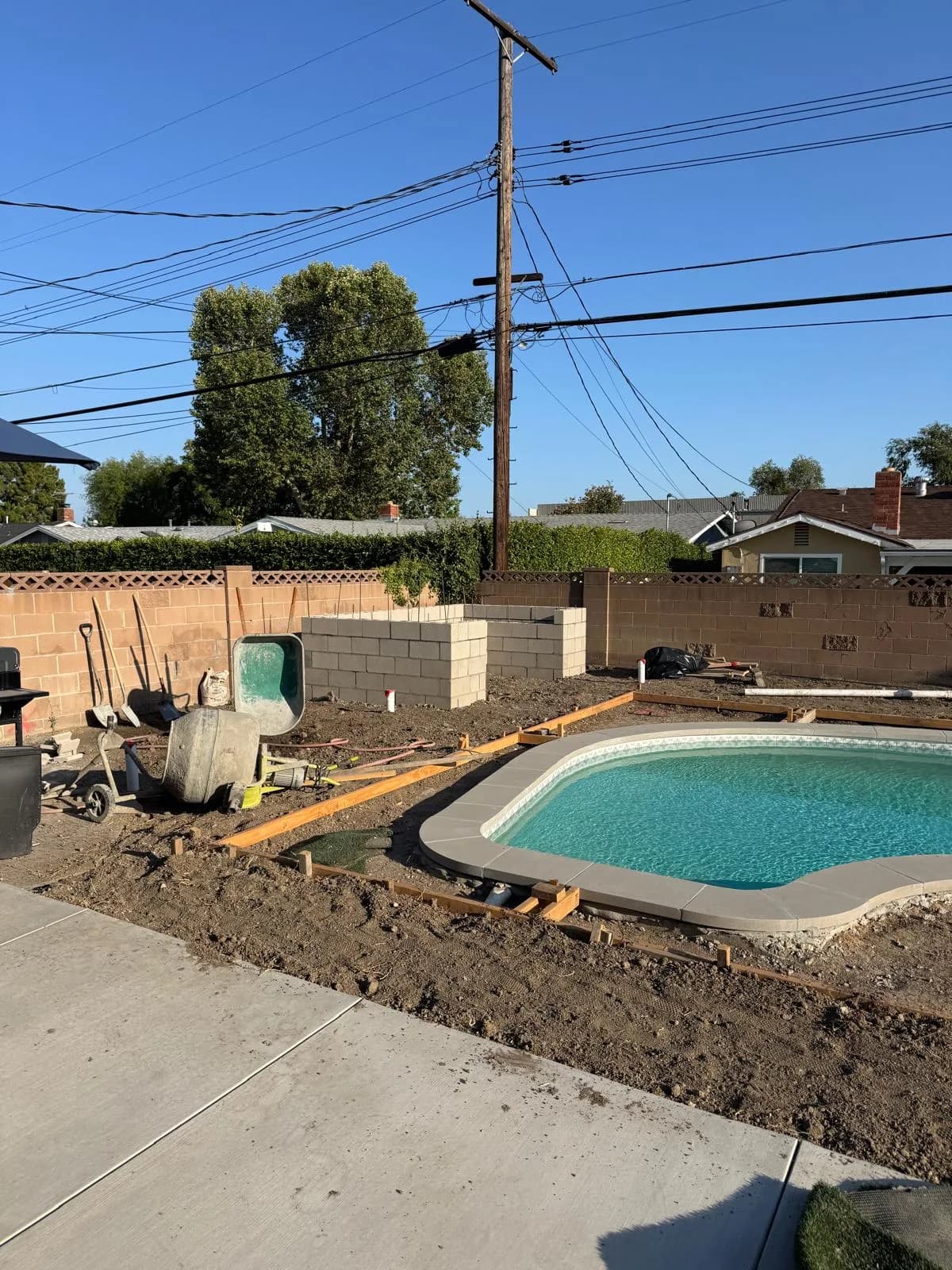 Pool remodel with new coping installed, water in the pool, and dirt grading around the deck area
