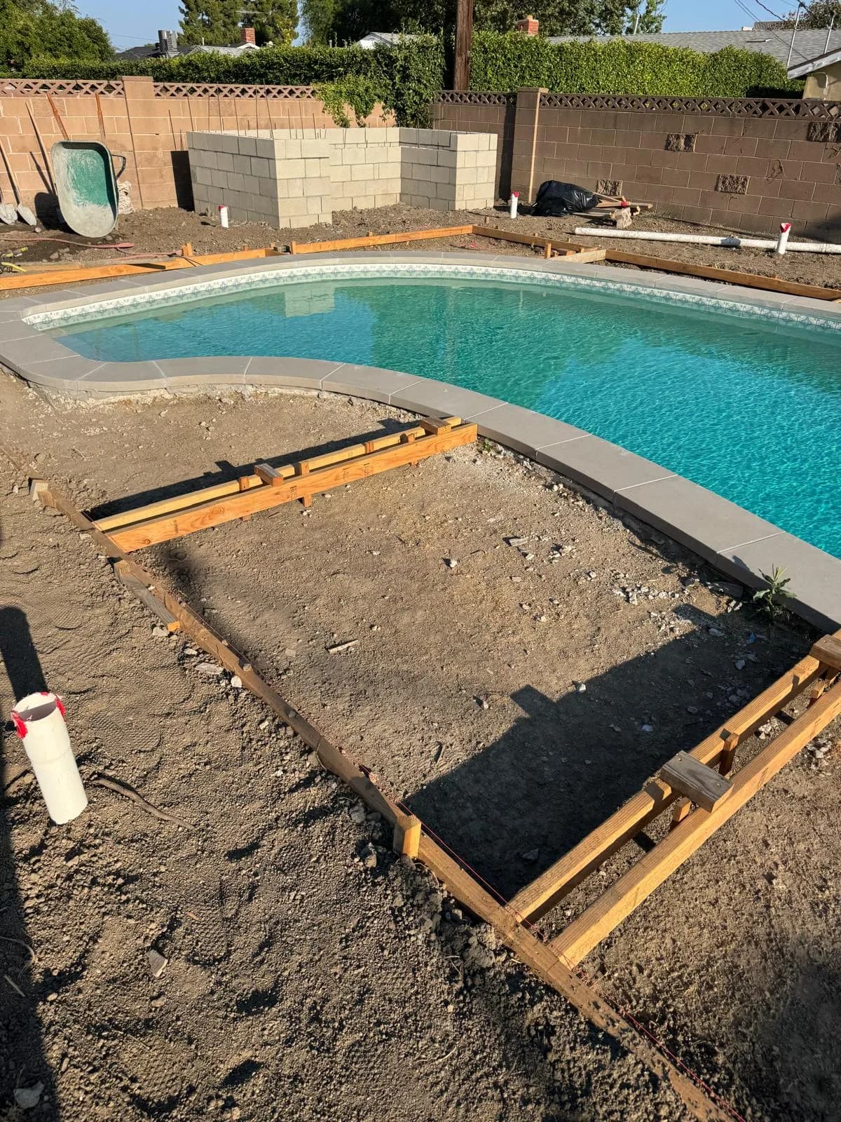 Refinished pool with new coping beside framed dirt areas prepared for surrounding deck work