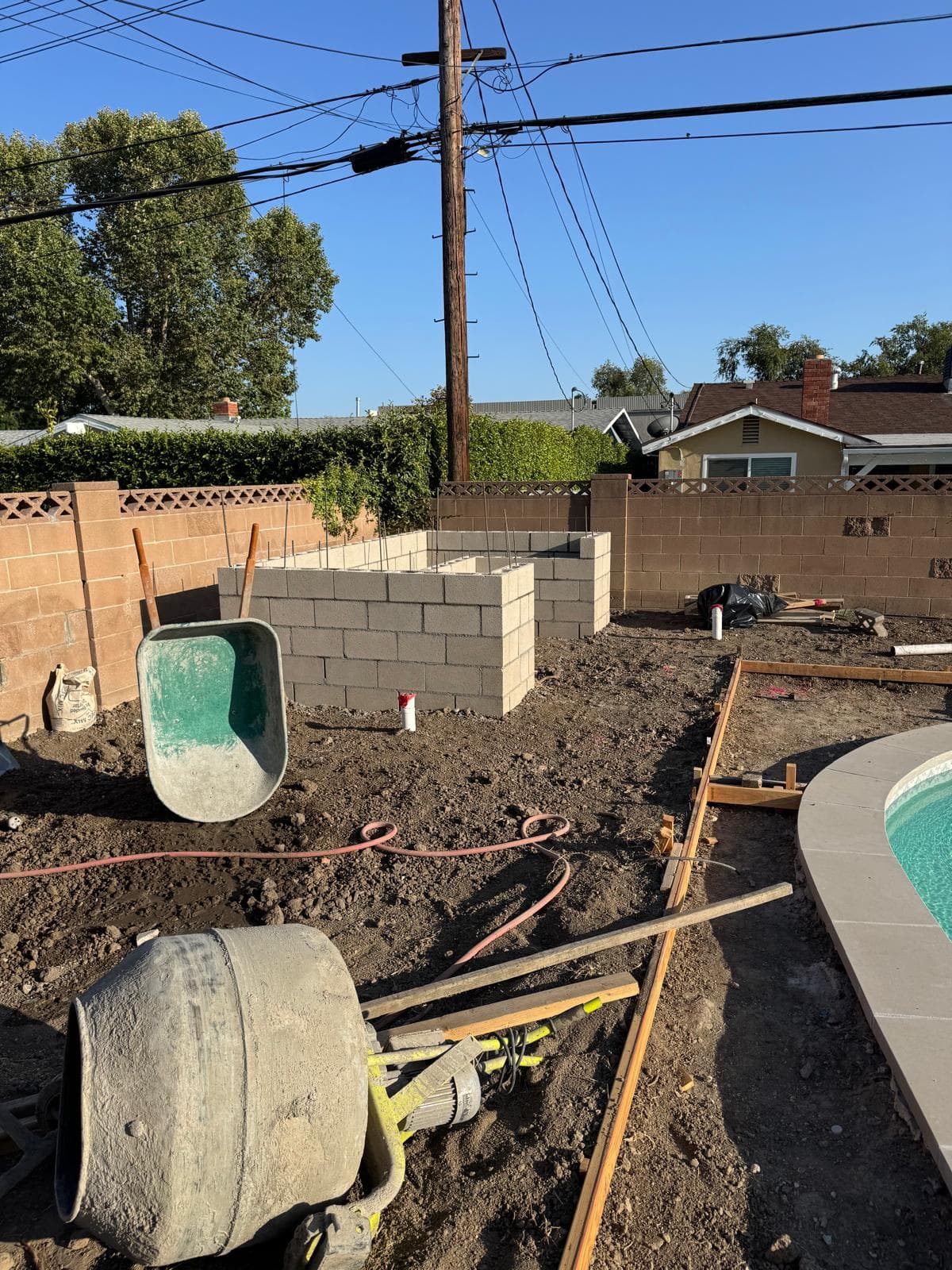 Backyard pool remodel with new cinder block structure, dirt grading, wheelbarrow, and forms beside the pool