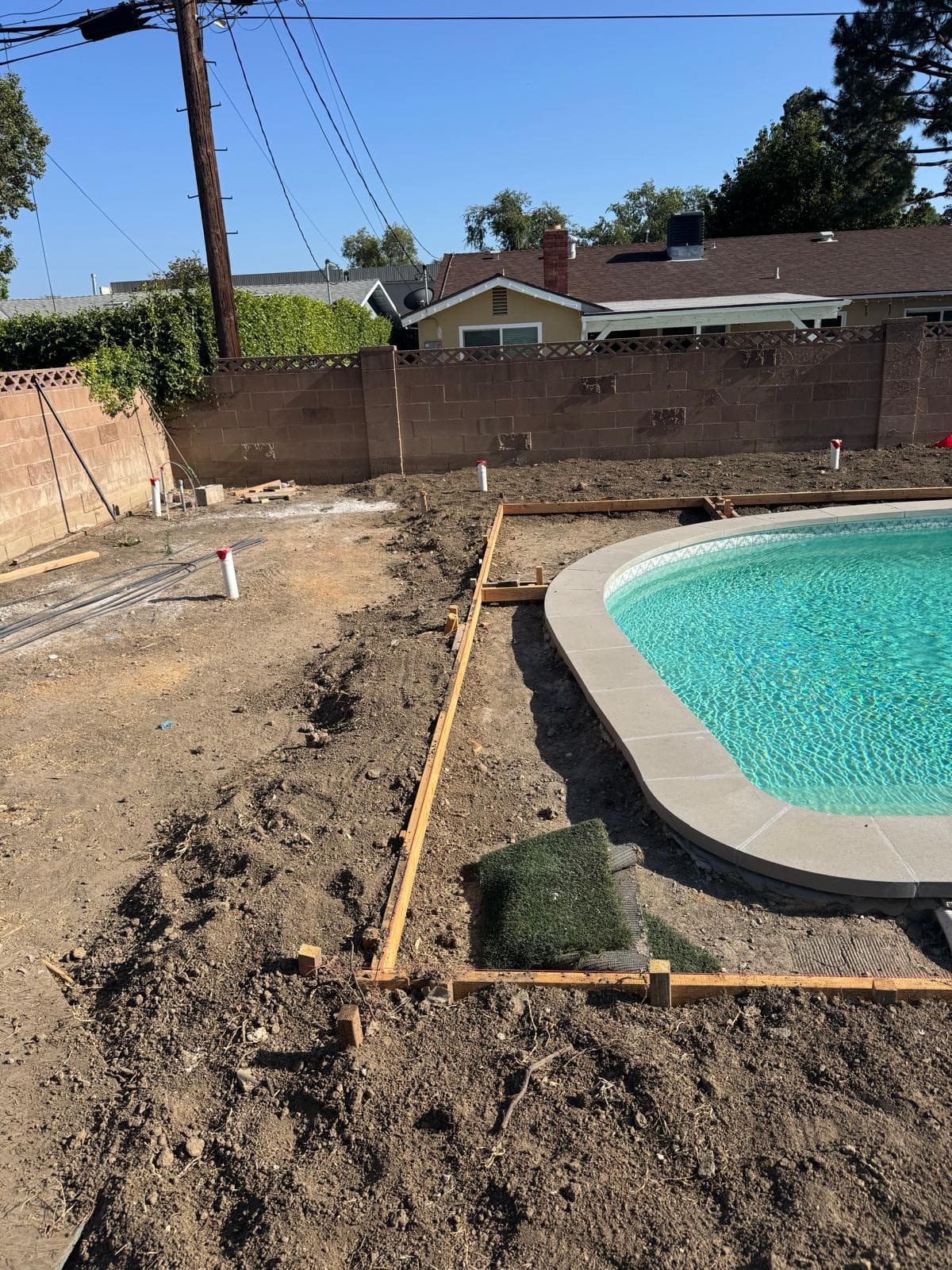 Pool with new coping beside excavated dirt and wood forms set for surrounding deck work