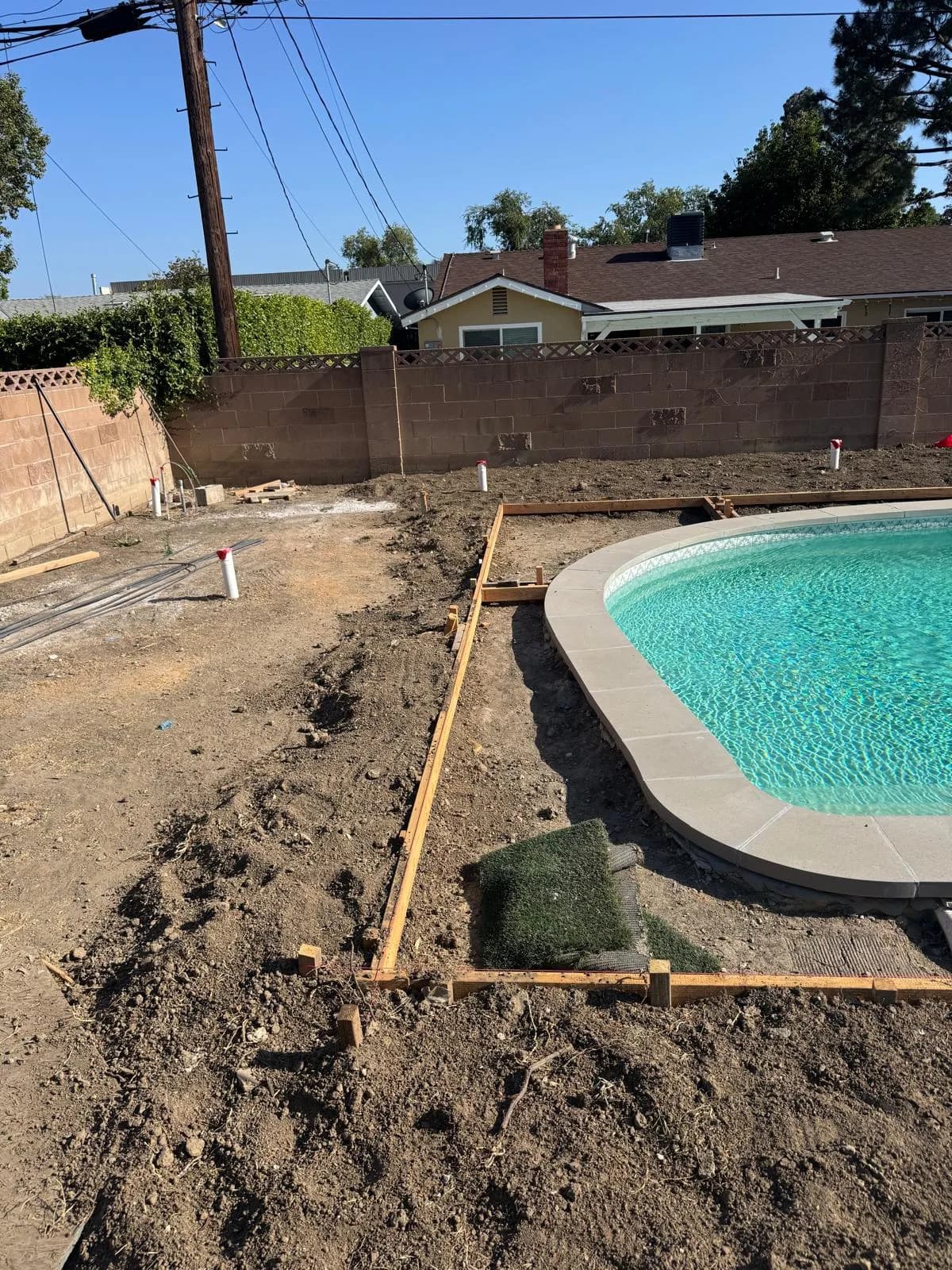 Pool with new coping beside excavated dirt and wood forms set for surrounding deck work