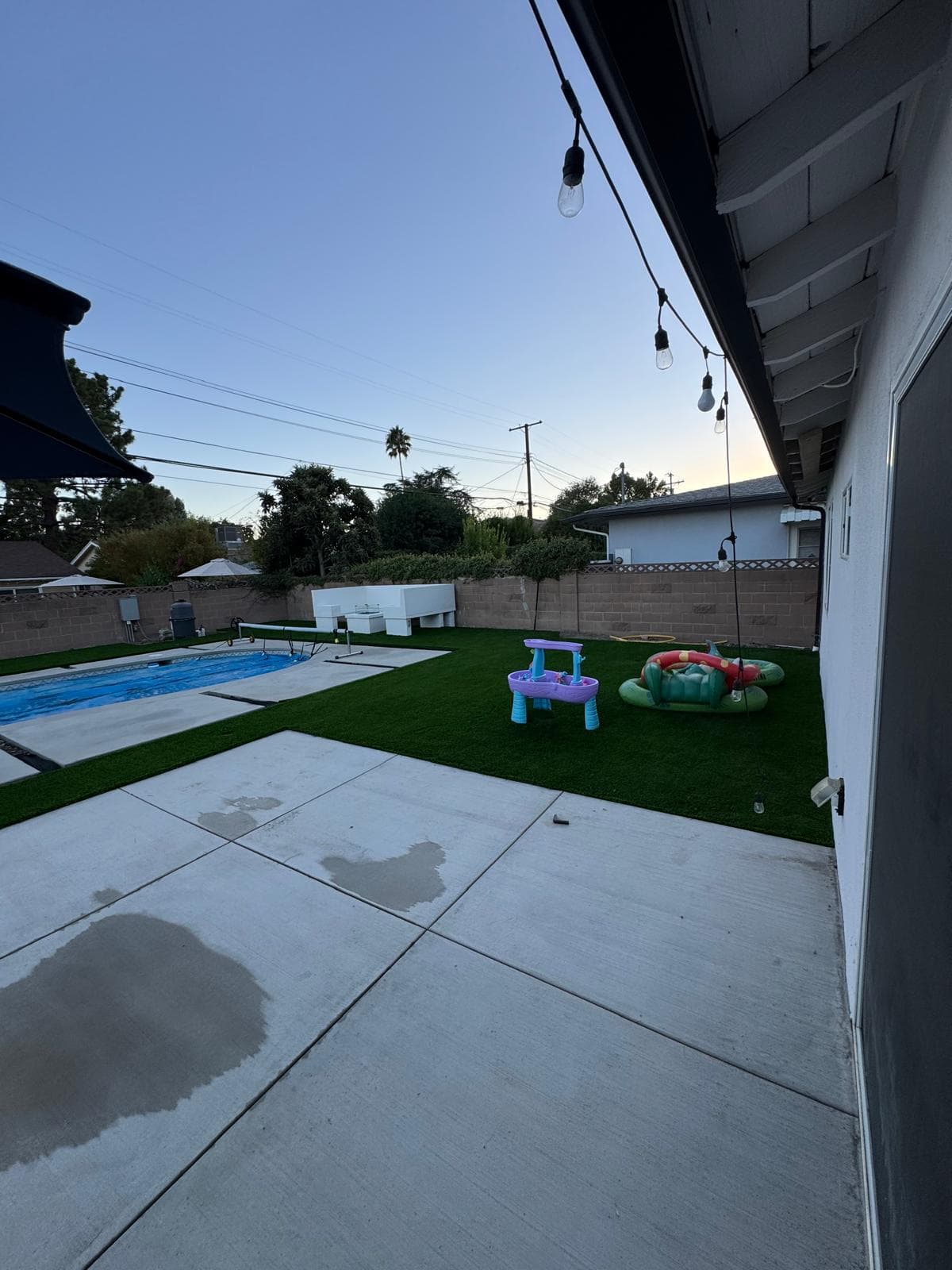 Backyard with a remodeled pool, new concrete patio, artificial turf, and children's play toys