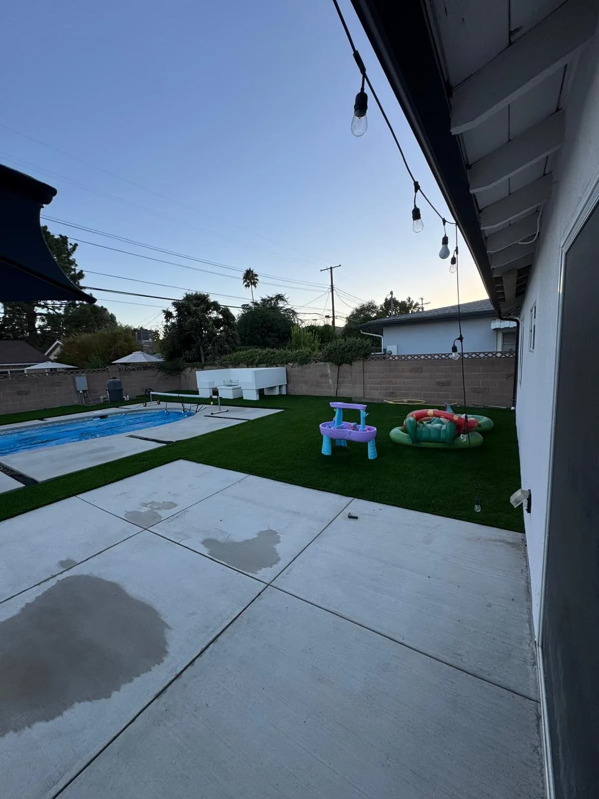 Backyard with a remodeled pool, new concrete patio, artificial turf, and children's play toys