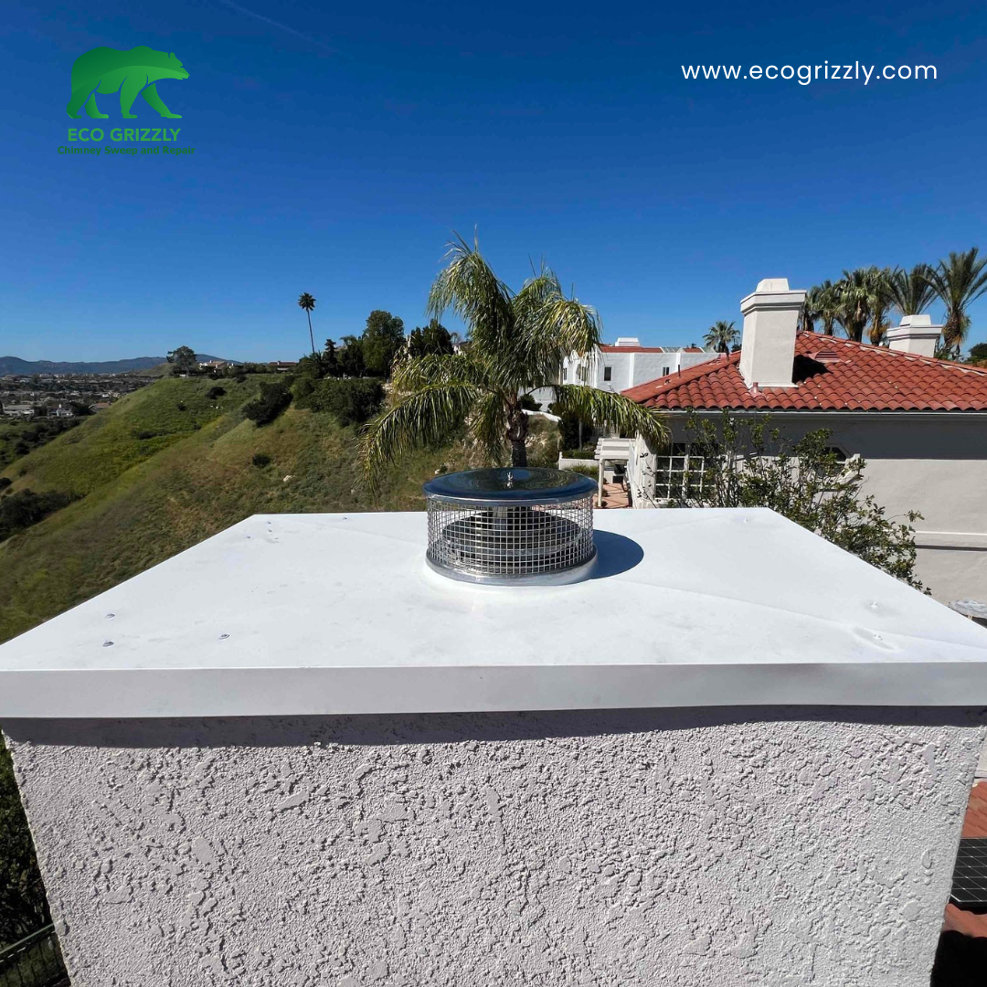 Stainless steel chimney cap with mesh screen installed on a white chimney crown in Southern California